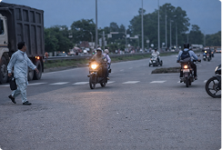 A pedestrian crossing a highway at dusk between moving motorcycles
