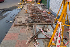 Broken footpath slabs and unguarded roadside excavation behind barricades