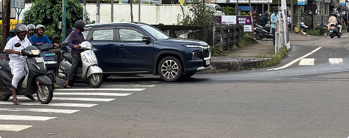 A car stopped across a zebra crossing while two-wheelers wait behind it